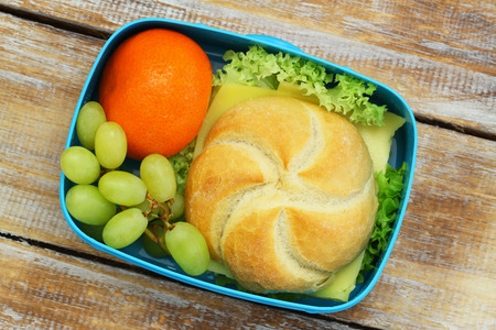 Lunch box containing cheese roll, mandarine and grapes on rustic wooden surfaceの写真素材