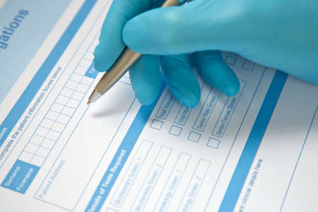 Health professional with blue gloves, completing pathology blood test request form.の写真素材
