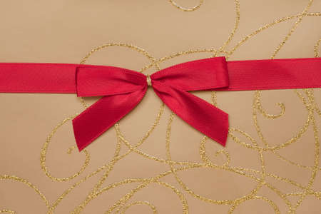 Detail of a parcel wrapped with gold paper and decorated with red ribbon.の写真素材