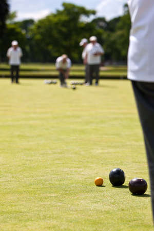 Men playing lawn bowls. Very narrow depth of field. Focus on the jack and woods. Distant player has just released wood.の写真素材