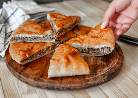 Traditional Ossetian meat pies with beef, on a wooden background. Rustic style, close up, selective focus with a female handの写真素材