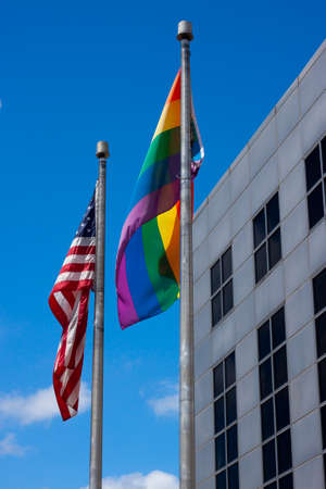 Maryland, USA 07/10/2020: An abstract concept image showing an American Flag and LGBT rainbow flag on side by side flag poles at full mast waving in the wind.のeditorial素材