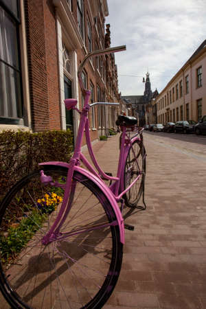 A close up view of a pink spray-painted vintage bike parked in a residential neighborhood in Amsterdam. Bicycle is operational with a dynamo and flashlight and adds a stylish look to the place.の写真素材