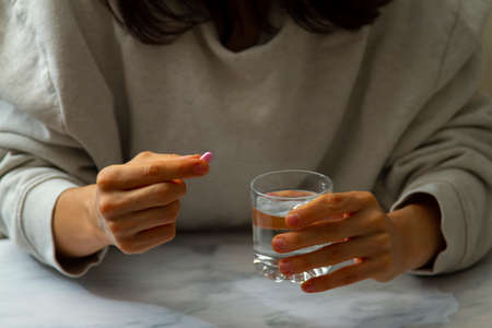 A woman is seen as she is holding a pill in one hand and a glass of water on the other hand. She is about to take the pill. A versatile image for multi purpose use in healthcare related issues.の写真素材