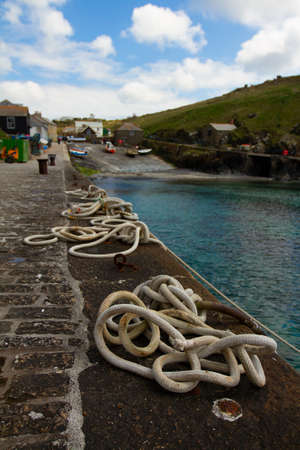 Close up image of tangled  mooring ropes tied to metal rings on a stone dock. These ship ropes are used to tie boats to the wharf in this small fishing harbor.の写真素材