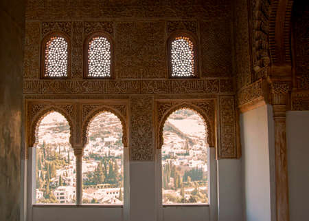 Granada, Spain 07/13/2010: Interior view of the famous Alhambra Palace featuring decorative Arabic letters and Islamic motifs carved on the stone wall. View of the city is seen through arched windows.のeditorial素材