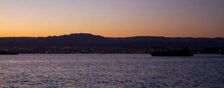 A sunset panorama showing the red horizon over the silhouettes of mountains of the coastal city of...