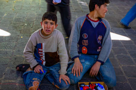 Damascus, Syria 03/28/2010: Teenager boy is sitting on his knees on cobblestone street floor of the Al Hamidiyah Souq (covered market) trying to sell plastic toys on a makeshift display.のeditorial素材