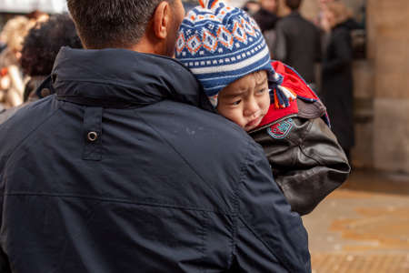 Oxford ,UK 02/27/2010: A close up image of a cute Asian baby. boy in winter clothing while being carried by his father. He looks tired and sleepy. He rests his head on the shoulder.のeditorial素材