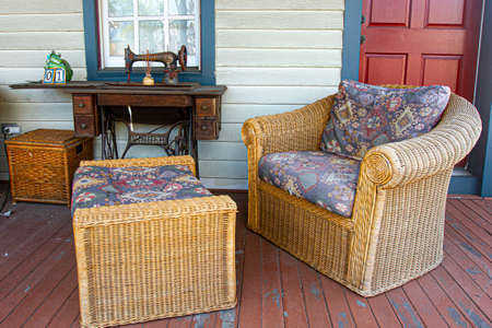 Chesapeake City, MD 08/25/2020: Outdoor seating arrangement on the aged porch of a 19th century American house. Image features straw mat chairs with pillows and an antique rusted Singer sewing machineのeditorial素材