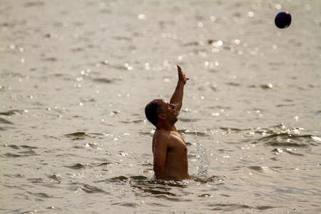 Rock Hall, MD 08/22/2020: A young caucasian man is playing a ball game in Chesapeake bay. He is...