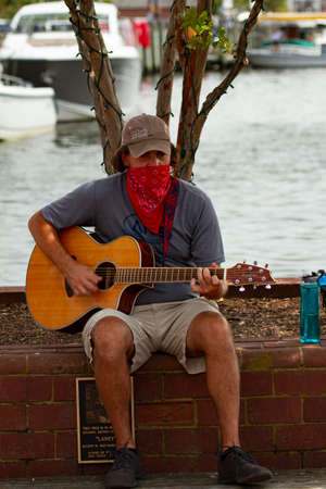 Annapolis, MD 08/21/2020: A young caucasian man is sitting on a brick wall in Annapolis marina and...