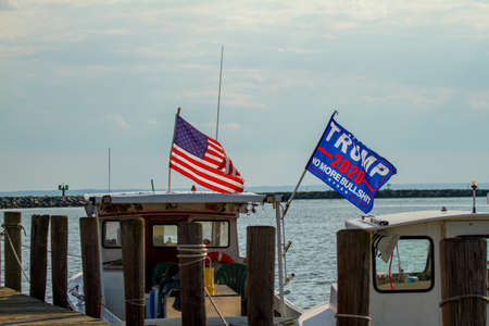 Rock hall, MD ,USA 08/18/2020: Trump 2020 flag waving on a flag post at the back of a boat. The flag has a slogan saying 'No More Bullshit'.  An American Flag is flying just next to it.のeditorial素材