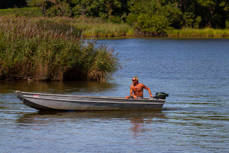 Eastern Neck Island, MD, USA 08/30/2020: A middle aged athletic shirtless caucasian man is  in a small aluminum fishing boat in Chesapeake bay. He is navigating the boat using the outboard engineのeditorial素材