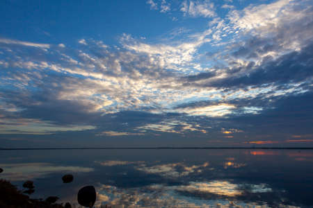 An abstract image taken at a lakefront at sunset. Image shows a spectacular cloudy sky and its...