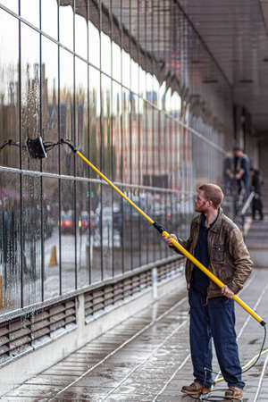 Oxford, UK, 12/09/2009: A caucasian man wearing boots, overalls and a leather jacket is cleaning the exterior windows of a building using a telescopic brush.のeditorial素材