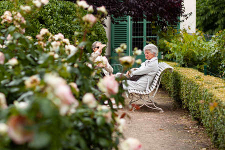 Paris/France 06/13/2010: Three elderly women are sitting on decorative benches in a rose garden and are having a friendly conversation while enjoying the beautiful weather.のeditorial素材
