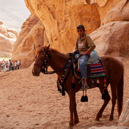 Petra, Jordan 04/02/2010: A local bedouin boy wearing jeans and sandals is on a horse with decorative mouth bit. They rest in the shade of a cliff in Petra.のeditorial素材