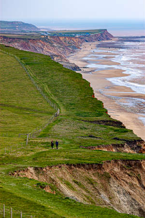 Isle of Wight, UK, 04/25/2010: atlantic coast of Isle of wight in spring. A grassland meadow on top of coastal cliffs, a hiking path with backpackers, people on the beach at distance are seen.のeditorial素材