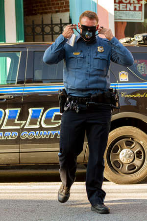 Ellicott City, MD, USA 10/07/2020: A young caucasian male police officer is crossing the street. He...