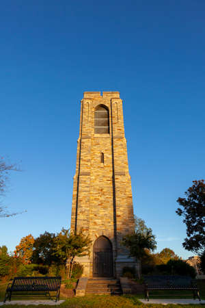 autumn image of the Joseph D. Baker Tower and Carillon at sunset located in Baker Park, Frederick. Low angle bug eye image has clear blue sky in background and park benches in foreground.の写真素材