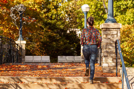 A young caucasian woman wearing floral shirt and jeans is climbing stairs in a city park. It is a...