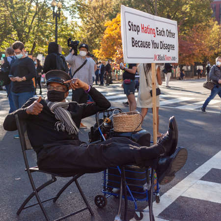 Washington DC, USA 11/06/2020: An elderly African American man is sitting next to a banner that says "Stop Hating Each Other Because You Disagree" A nice message to relieve political tension in DC.のeditorial素材