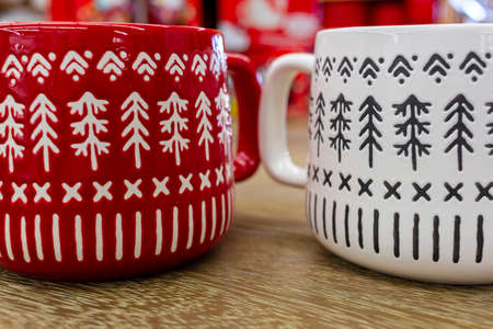 Closeup image of two (red and white) porcelain coffee mugs placed on top of a wooden table. Both...