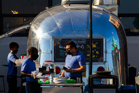 Alexandria, VA, 11-28-2020: Riverside Taco Company: A shiny metal food truck decorated as a stylish take away taco van restaurant parked in the waterfront of Alexandria. Employees wear face mask due to COVID 19 pandemic.のeditorial素材