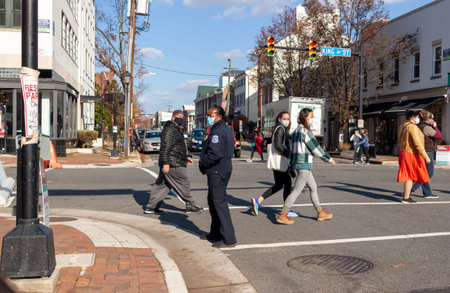 Alexandria, VA, USA 11-28-2020: A group of men and women are crossing the street while an African American female police officer is controlling the traffic. Everyone is wearing face masks due to COVIDのeditorial素材