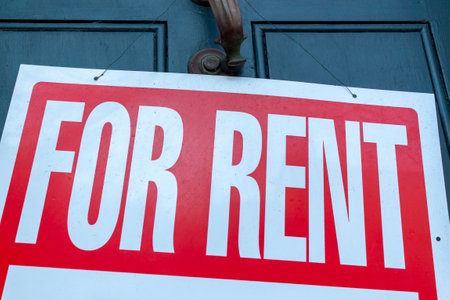 A large For Rent sign (white text on red background) is attached to  metal door handle on the front door of an old townhome. A versatile image for real estate, housing market, economy related themes.の写真素材