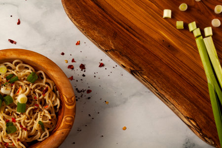 A wooden bowl of cooked ramen noodles seasoned with herbs and freshly chopped spring onionsの写真素材