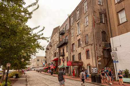 Savannah, GA,USA 07-04-2018: View of the old town historic district of picturesque Savannah with tourists walking on cobblestone streets, local shops and rundown vintage apartments on sides.のeditorial素材