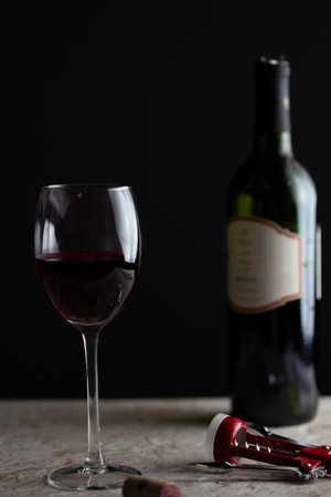 Image of a standard size wine glass with red wine filled halfway through. There is a corkscrew on...