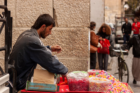 Damascus, Syria 03-28-2010: A young Arabic man is selling gummy candies on a food cart on the street in the old city of Damascus. Piles of assorted sweets are displayed without hygienic measuresのeditorial素材