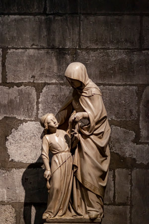 Paris, France 06-12-2010: An ancient marble sculpture depicting mother and child inside the famous Notre Dame Cathedral of Paris. It is a low light image with a wall behind.のeditorial素材