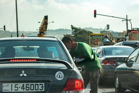 Amman, Jordan 03-29-2010: A poor young refugee boy is begging at the traffic light on a crowded road in Amman. The young Arabic man taps on window of cars stopping at red light and asks for money .のeditorial素材