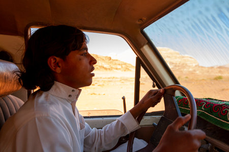 Wadi Rum, Jordan 03.31.2010: A local beduin tour guide is driving a vintage off road vehicle during a desert safari tour in Wadi Rum Desert in Jordan. The Arabic boy wears traditional jubba thobe.のeditorial素材