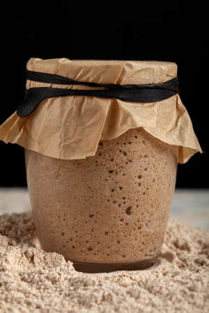 A glass cup of sourdough starter culture for homemade bread making. The cup is covered with brown...