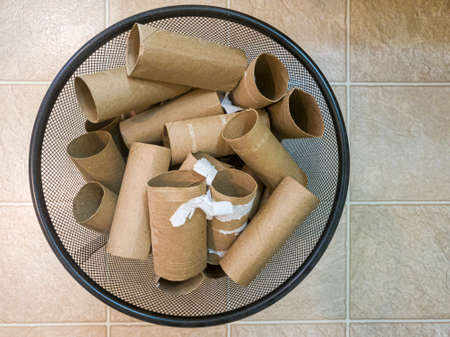 Flat lay top view image of a metal trash bin full of empty toilet paper rolls with some paper leftovers stuck on them. A concept image for buying, hoarding running out of toilet papers or recycling itの写真素材