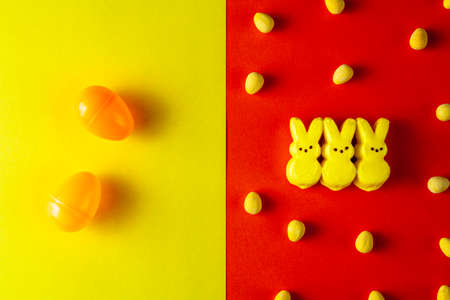 Flat lay view of Three little glazed marshmallow easter bunnies  in the middle with multiple crisp sugar coated easter eggs scattered around. Easter celebration concept. Yellow over orange background.の写真素材