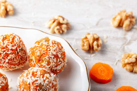A kitchen countertop with a flat porcelain plate. Homemade fresh carrot bliss balls (mixture of cookie crumbles, walnut and carrot puree) coated with coconut shred are served on the plate.の写真素材