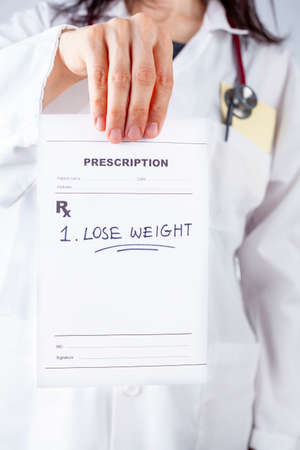 A caucasian female physician in white coat is prescribing Lose weight to an obese or overweight patient in her office. A concept image for lifestyle modifications, obesity, weight gain, problems,の写真素材