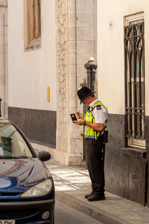 07-10-2010 Gibraltar, UK : A male police officer working at Royal Gibraltar Police (RGP), the main law enforcement agency in UK overseas territory Gibraltar is issuing a parking ticket on the streetのeditorial素材