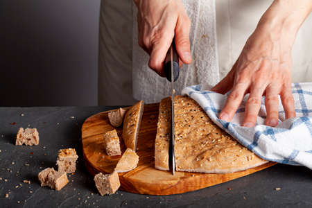 A woman chef is slicing fresh baked homemade Turkish Flat bread known as pide or pita on wooden chopping board. The wholegrain pita bread is round with poppy seeds and sesame seeds used as topping.の写真素材