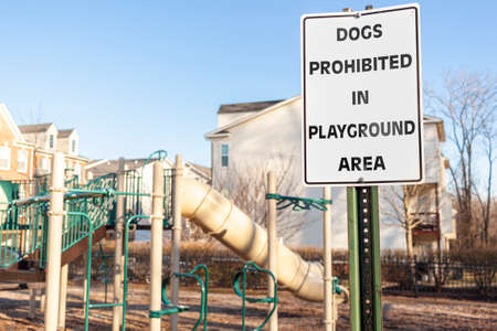 Dogs Prohibited in Playground Area Sign in front of the fences at a fenced playground of a residential suburban neighborhood. Pets may cause disturbance and scare kids during their exercise and play.の写真素材