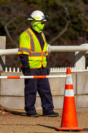 A construction worker wearing full protective gear including helmet, reflective vest, boots, gloves,...