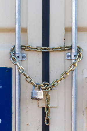 A heavy duty industrial size padlock was attached to steel chains at the entrance of an outdoor container that stores tools and equipment. Versatile image for locking, safety, security related conceptの写真素材