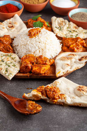 Angled image of a gourmet mixture of indian dishes including rice, naan, tikka masala, butter...