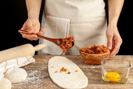 A Turkish woman is preparing kiymali pide, traditional flatbread with ground meat paste onto flattened dough and egg is spread on top of the mixture before baking in brick oven.の写真素材